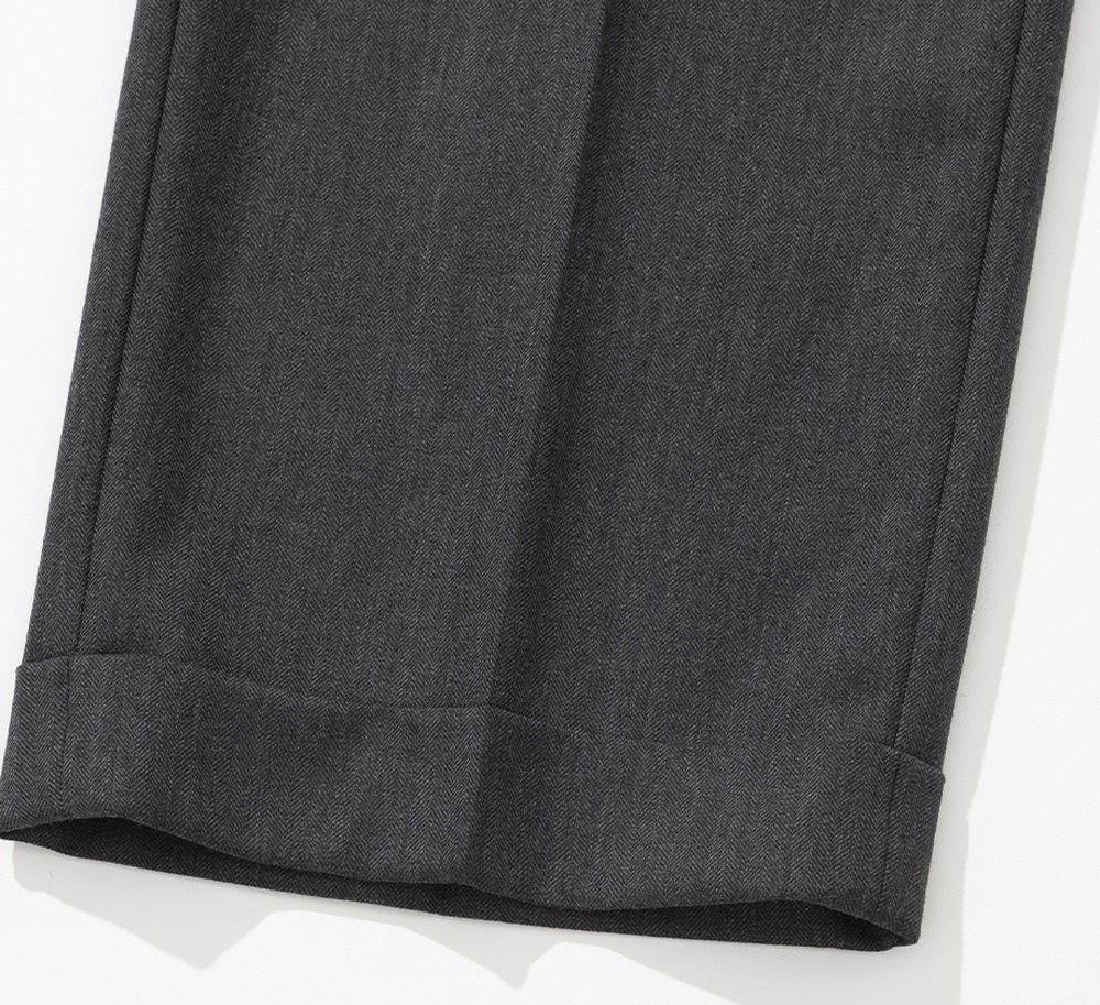 Close-up of a turn-up cuff on charcoal herringbone wool trousers, showing the folded band standing off the hem