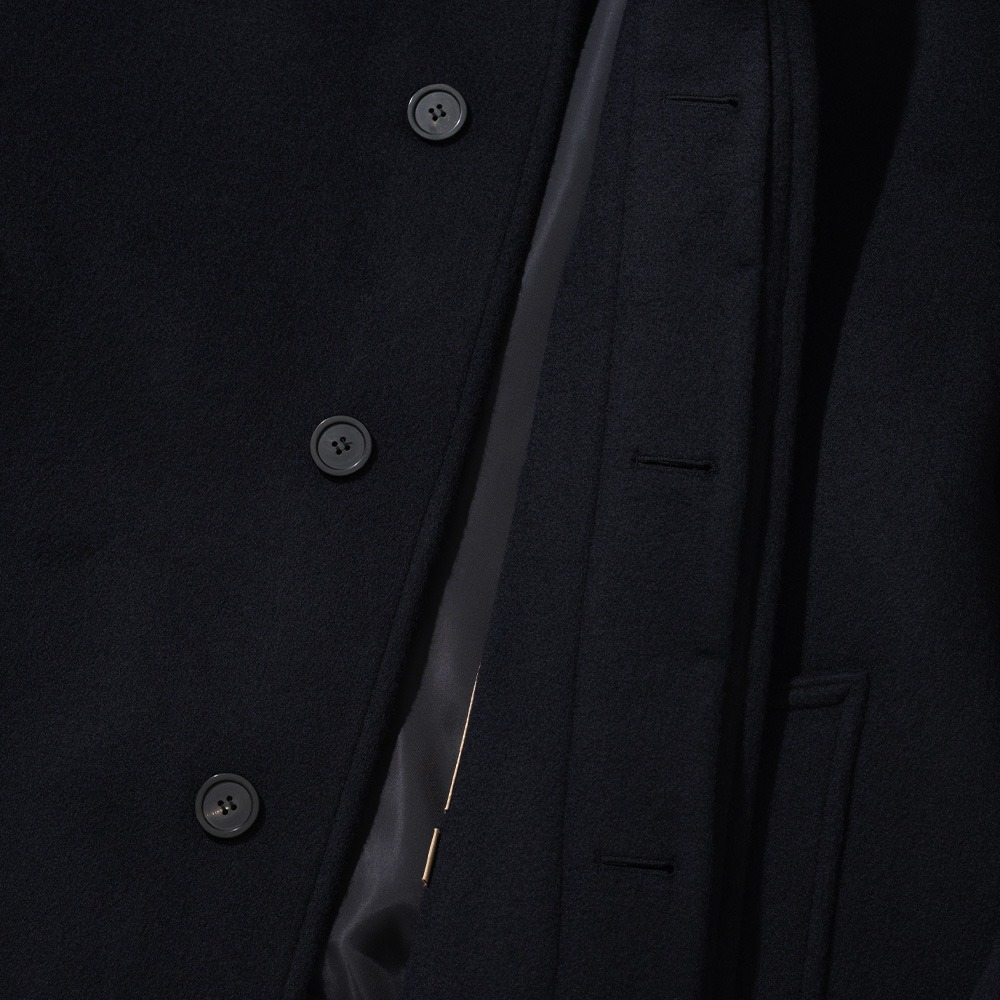 Close-up of the inside of a navy balmacaan coat's fly front, showing three buttons hidden behind the placket with the lining visible
