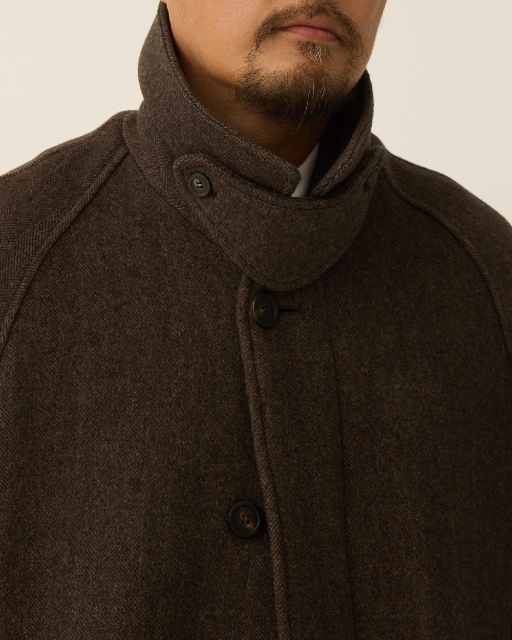 Close-up of a man in a brown herringbone balmacaan coat with the collar turned up and the throat latch closed