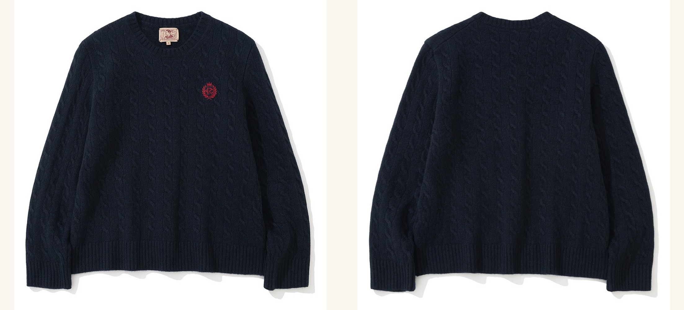 Navy cable knit crewneck sweater laid flat, front and back side by side: a small red embroidered crest on the chest at the front, plain cable columns across the back