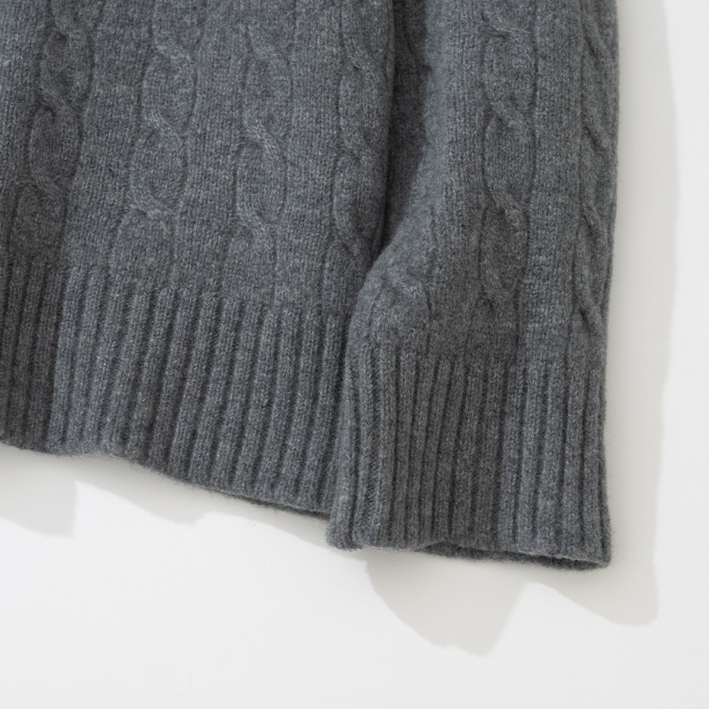 Detail of the ribbed cuff and hem of a grey cable knit crewneck sweater laid flat