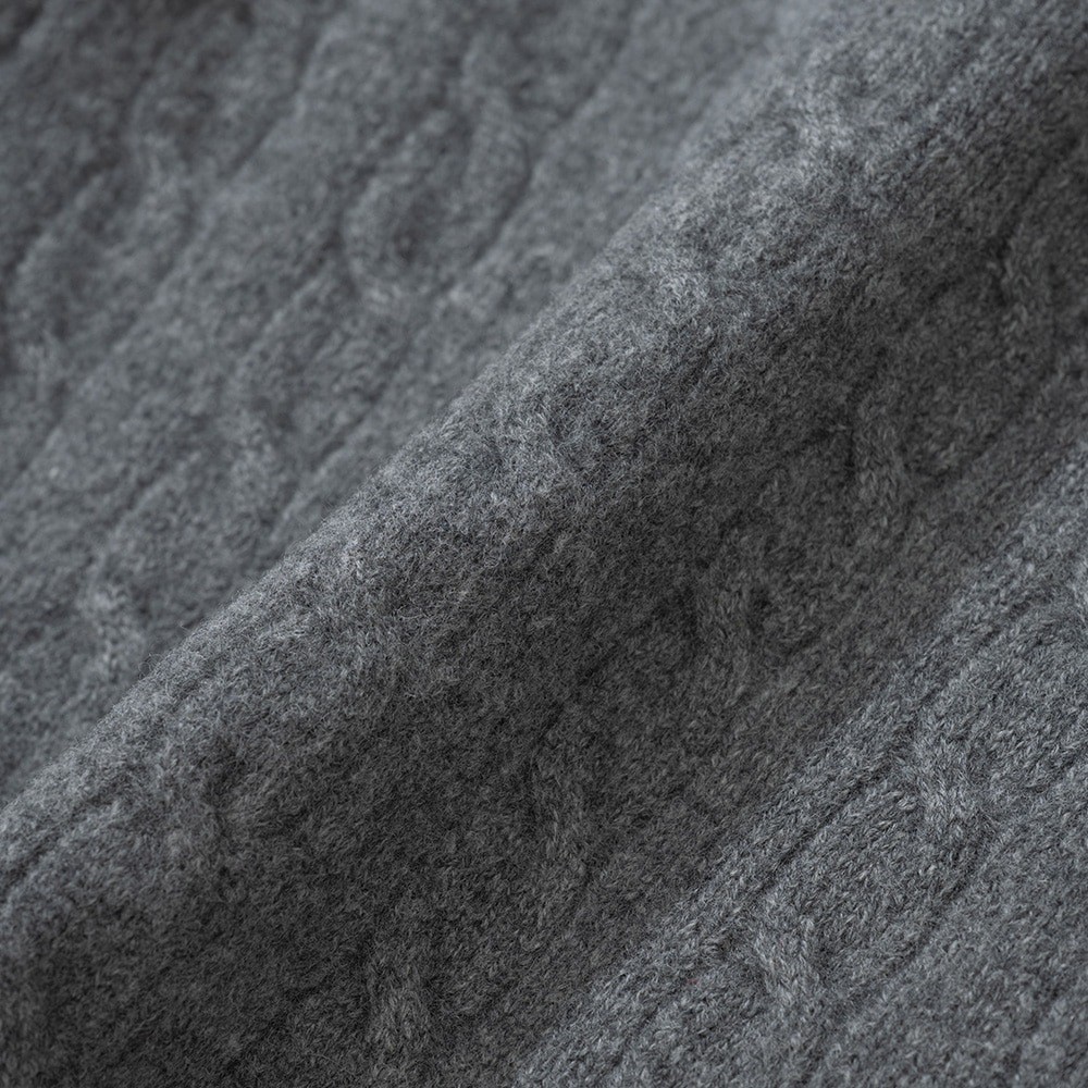 Macro view of a grey cable knit sweater in brushed merino wool, with twisted cable columns running diagonally across the frame