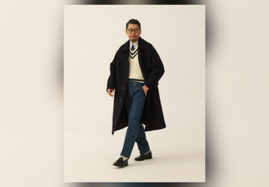 Navy Balmacaan over an ivory cricket sweater, shirt and tie, blue jeans and black loafers.