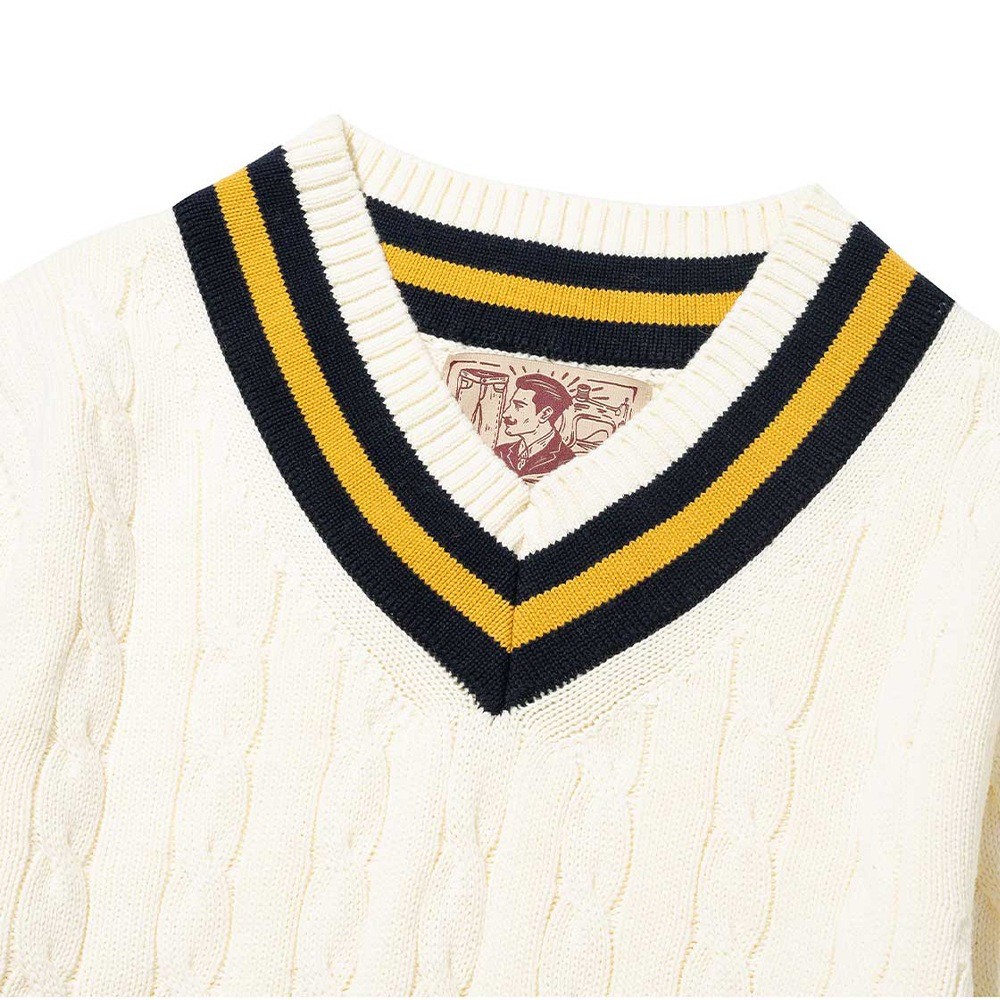 V-neck of an ivory cotton cricket sweater with navy and yellow stripes along the neckline and cable columns running down the front