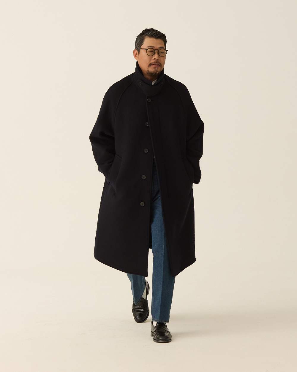 How to wear an overcoat casually: a navy Balmacaan with blue jeans and black loafers.