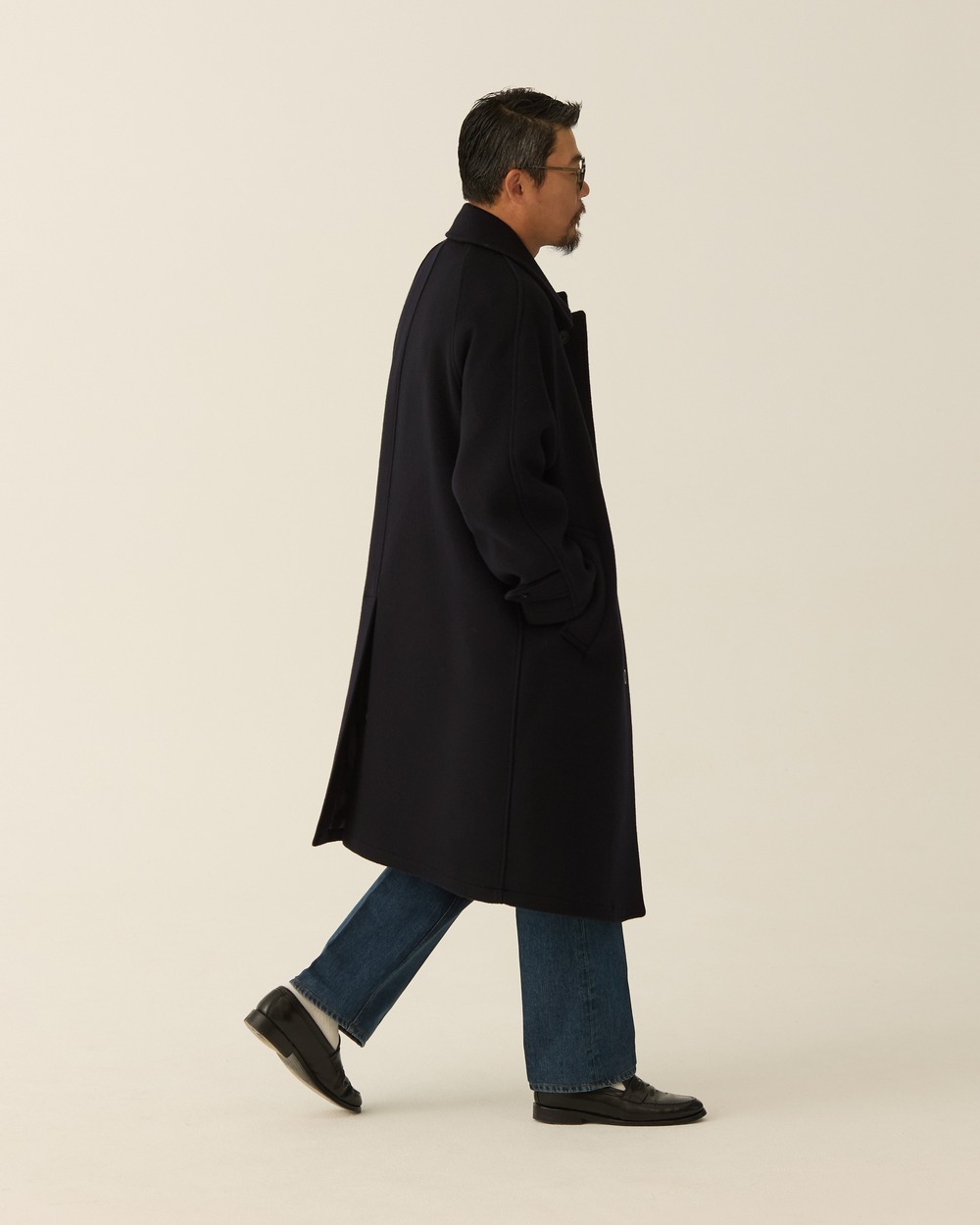 Side view of the navy coat with jeans, showing the hem during a stride.