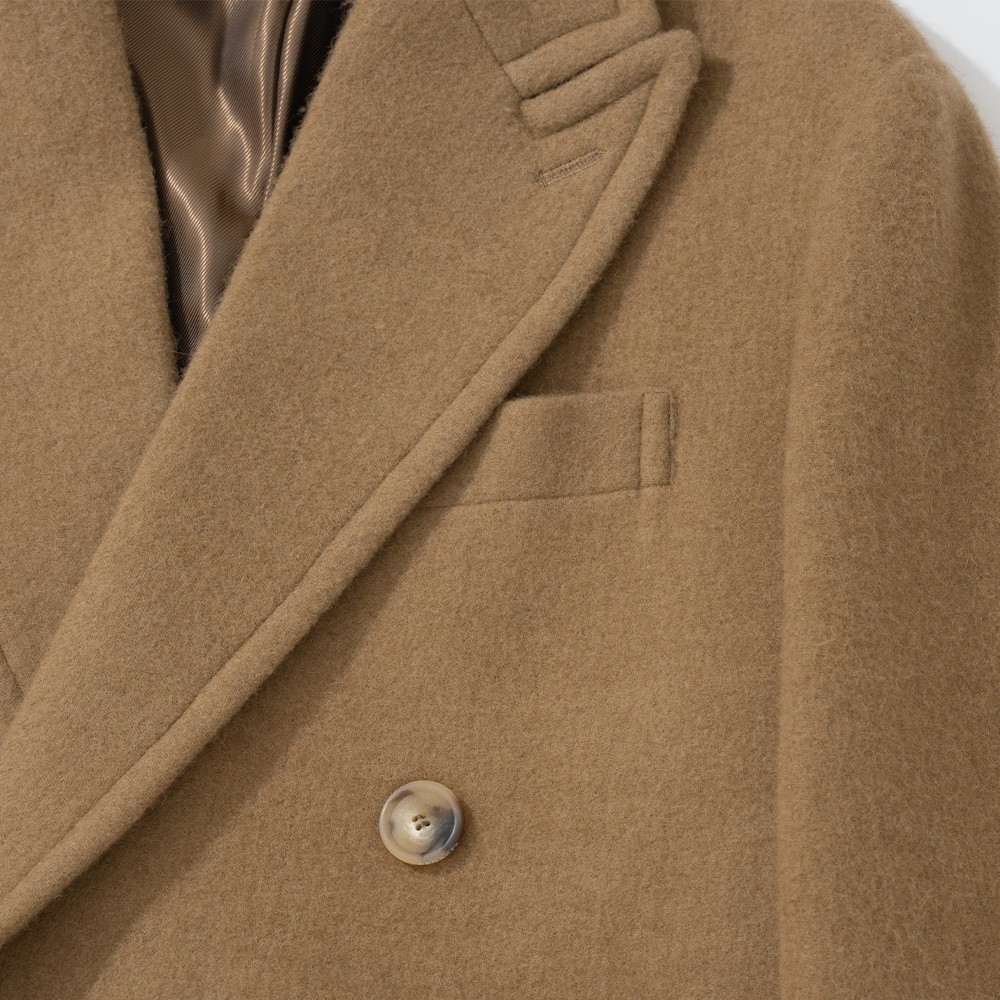 Close-up of the welt chest pocket on a camel polo coat, with the edge of the peaked lapel beside it