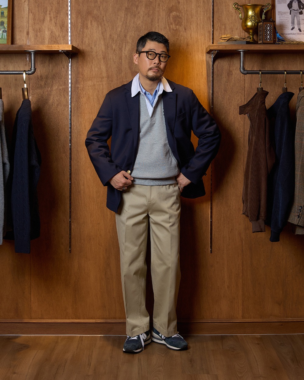 Man in a menswear shop wearing a navy blazer over a grey rugby collar sweatshirt, a light blue oxford shirt, khaki chinos and navy canvas sneakers