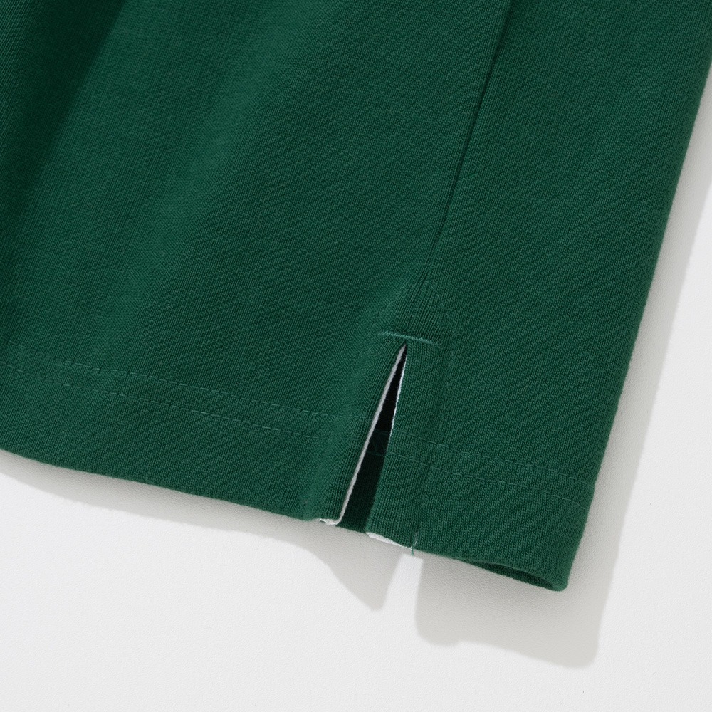 Close-up of the side vent at the hem of a green rugby shirt, with a small folded opening in the heavy cotton jersey